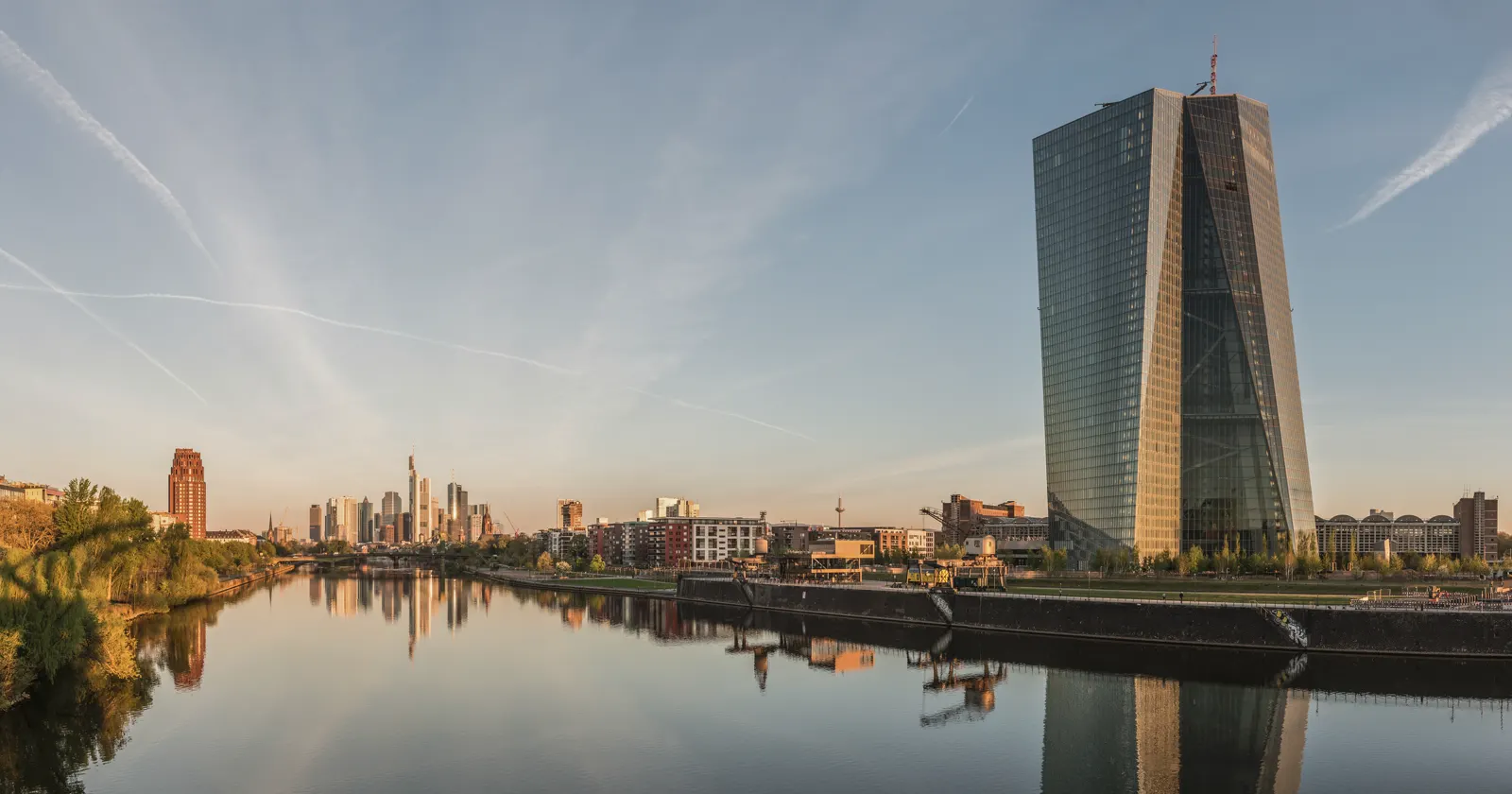 La torre del Banco Central Europeo al amanecer, reflejada en el río Meno, con el perfil de Fráncfort al fondo
