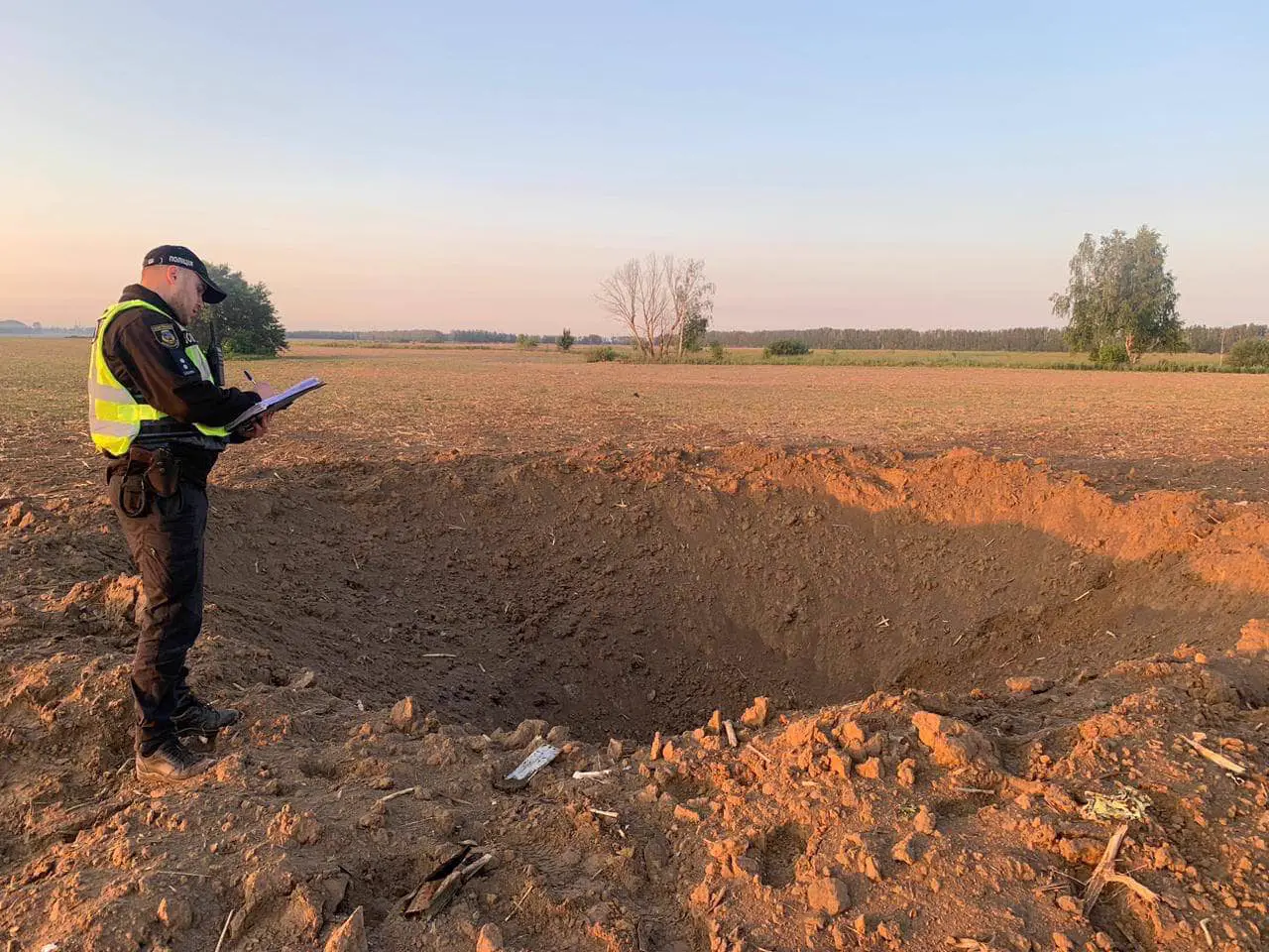 Un policía ucraniano con chaleco reflectante toma notas junto al gran cráter abierto por un impacto en un campo de labor de la región de Kiev.