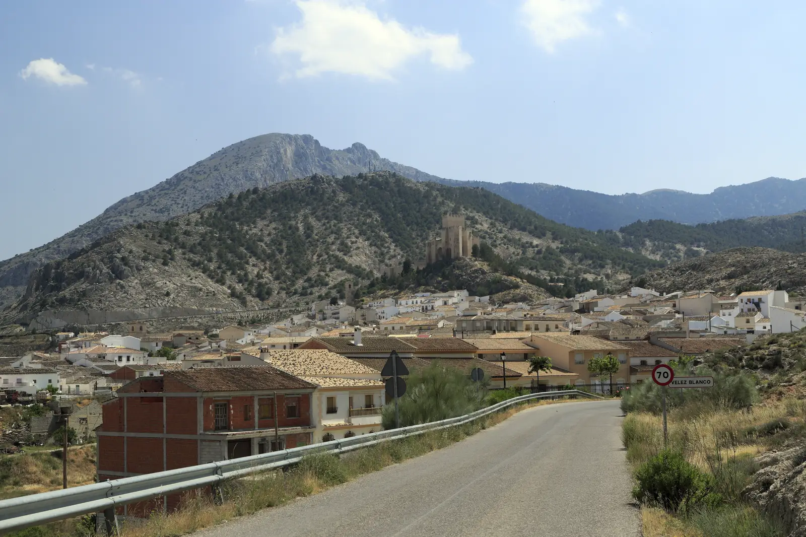 Carretera de entrada a Vélez-Blanco, con el pueblo blanco al pie de una sierra pelada y el castillo en lo alto de un cerro