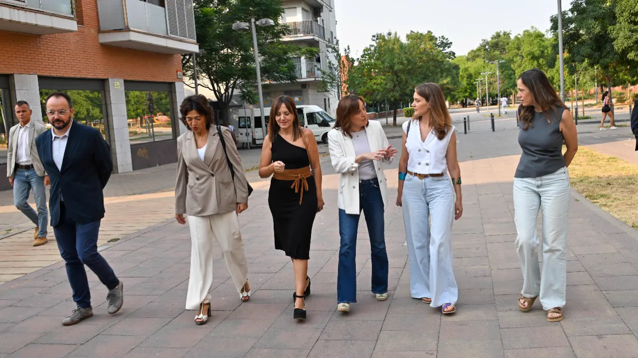 Seis personas caminan por una acera arbolada de Mollet del Vallès, frente a bloques de viviendas con locales comerciales cerrados en la planta baja.