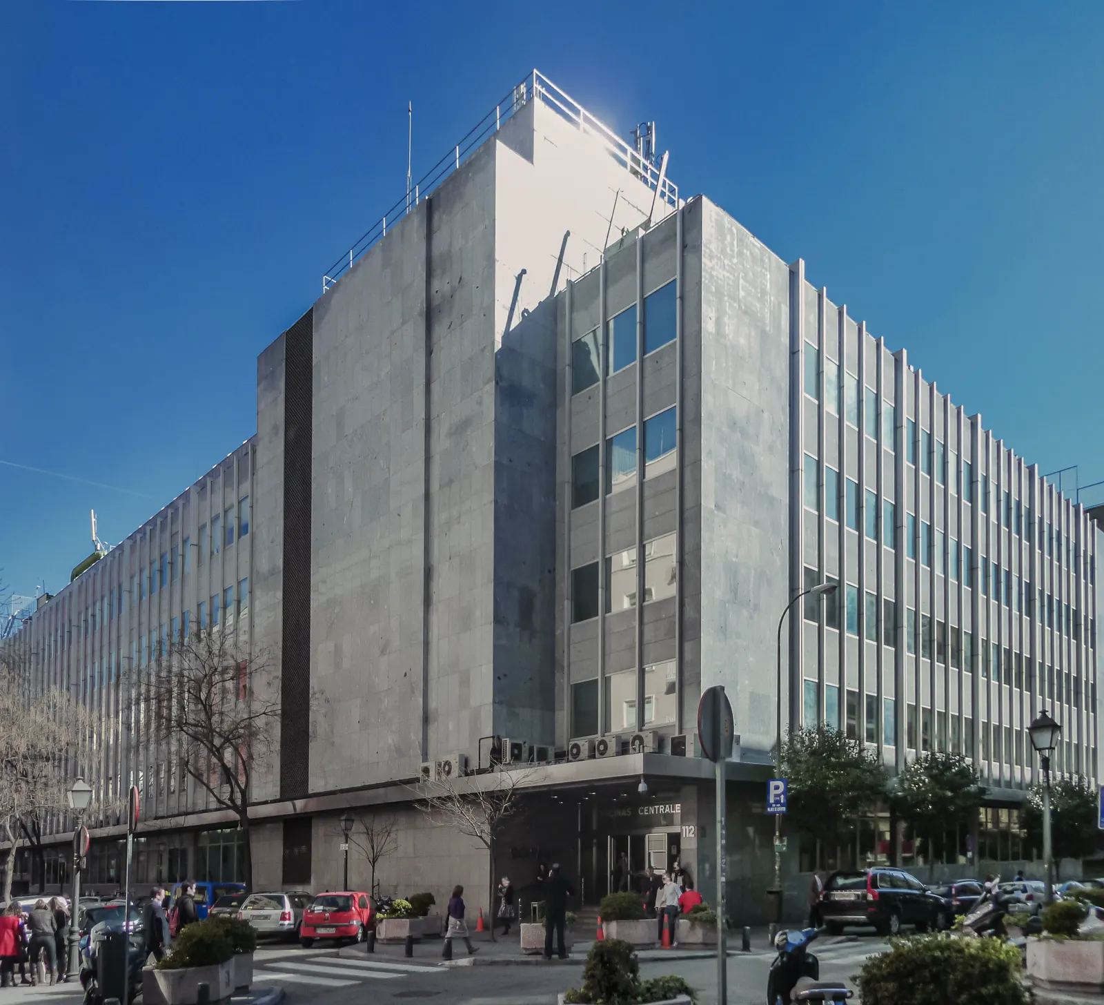 Edificio de oficinas de varias plantas, de piedra gris y ventanales verticales, en una esquina de una calle de Madrid, con el rótulo «Oficinas Centrales» y el número 112 sobre la puerta de entrada.