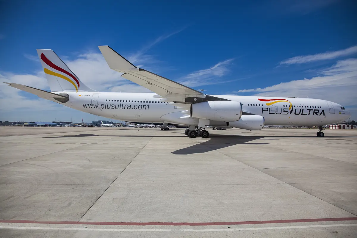 Airbus A340 blanco de Plus Ultra Líneas Aéreas, con matrícula EC-MFA y la dirección plusultra.com rotulada en el fuselaje, estacionado en una plataforma de aeropuerto bajo un cielo azul.