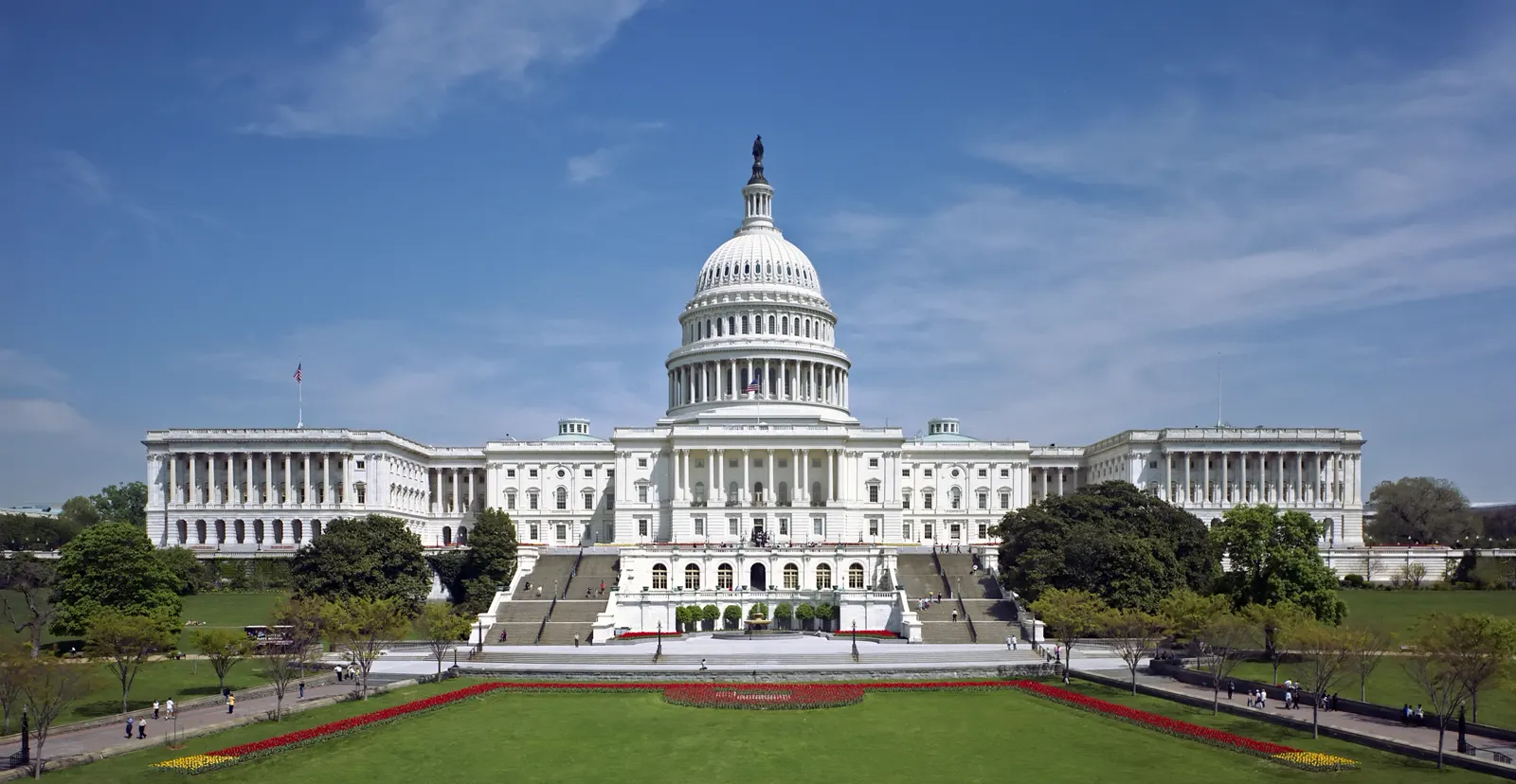 Fachada oeste del Capitolio de Estados Unidos en Washington, con su cúpula blanca y las escalinatas, bajo un cielo azul.