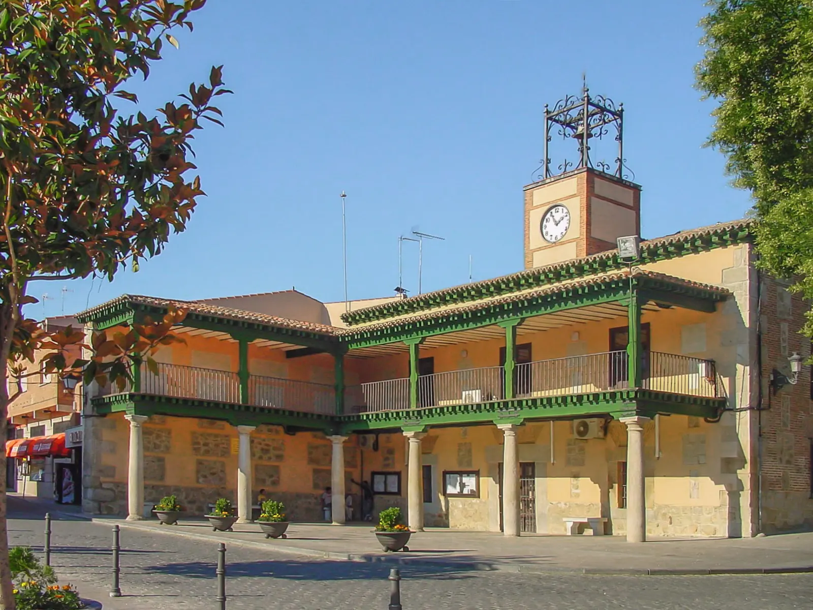Fachada del Ayuntamiento de Villa del Prado, edificio de piedra con soportales, bajo un cielo azul.
