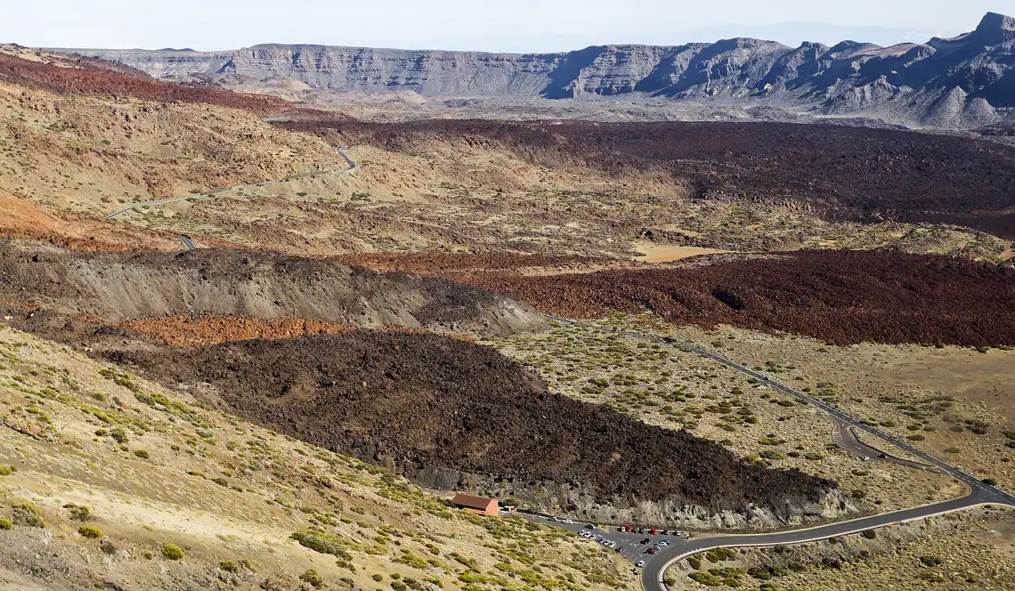 Vista panorámica del interior de la caldera de Las Cañadas del Teide, con coladas de lava oscuras, terreno ocre y la pared rocosa de la caldera al fondo