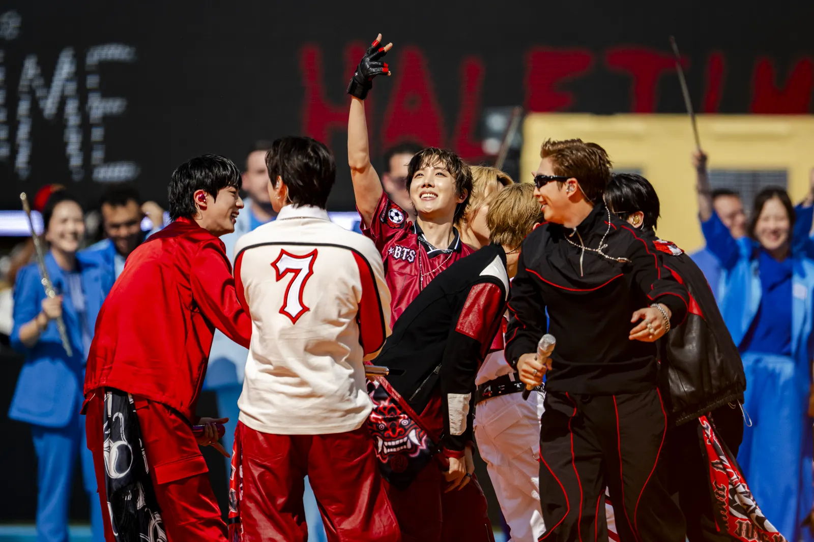 Los integrantes de BTS, vestidos de rojo y negro, celebran sobre el escenario del espectáculo del descanso