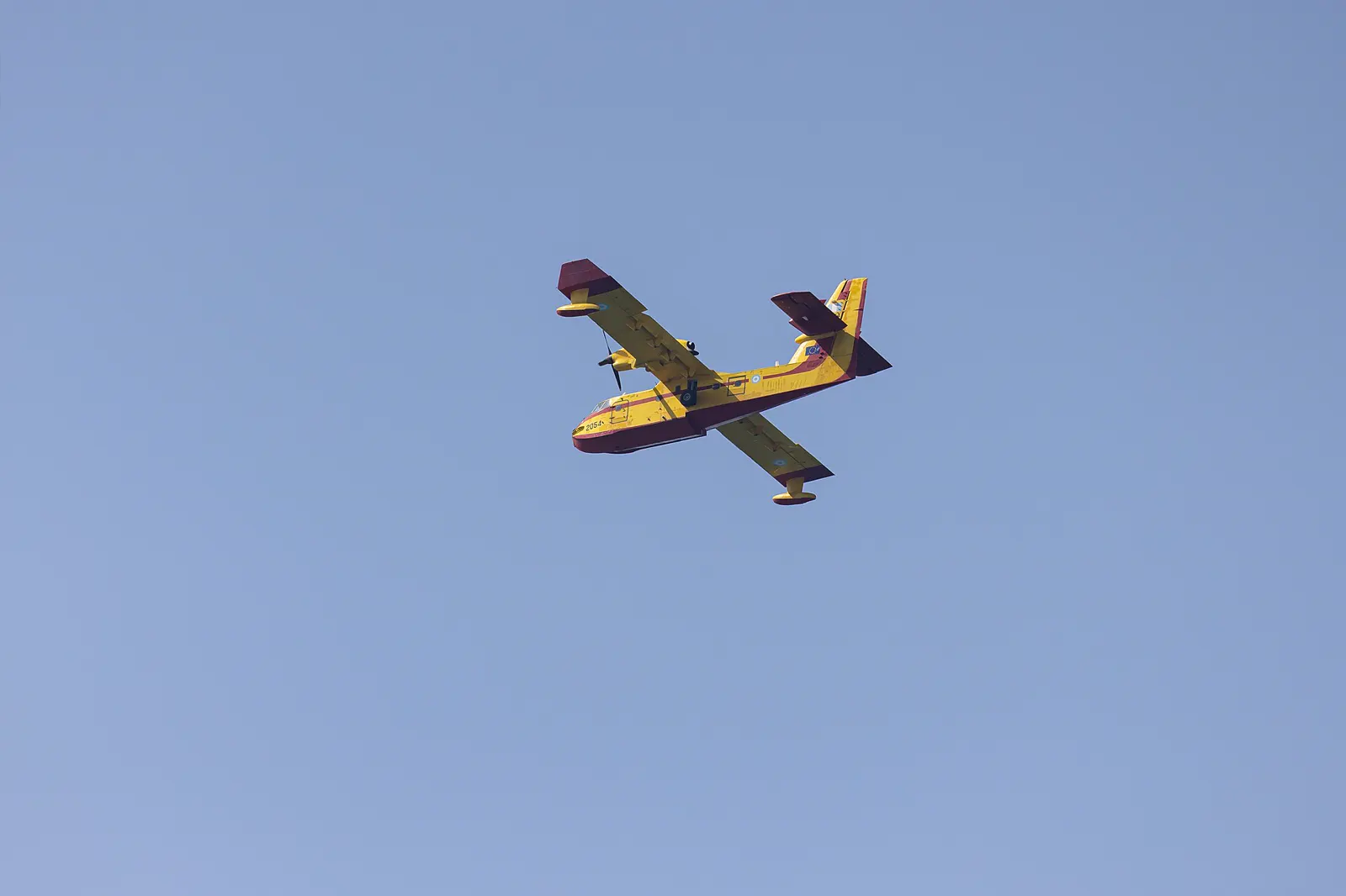 Avión anfibio Canadair CL-415 de la Fuerza Aérea Helénica, pintado de amarillo y rojo, volando contra un cielo azul despejado.