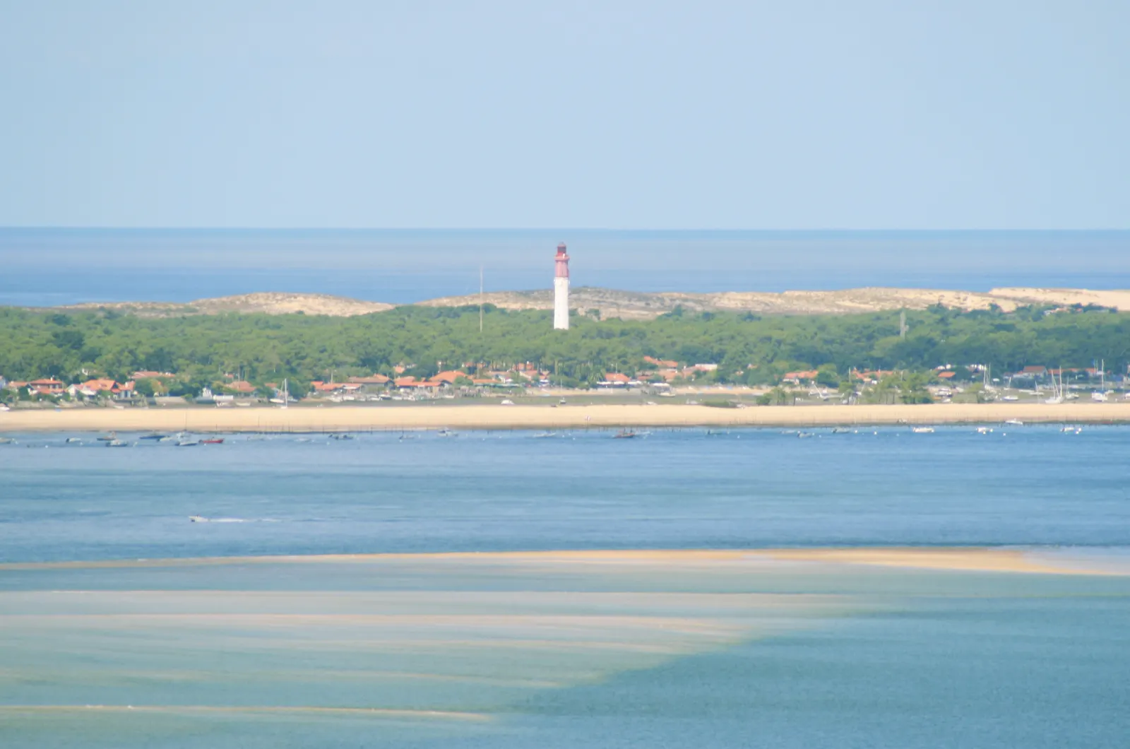 Vista aérea de la península de Cap Ferret con su faro blanco y rojo, el bosque de pinos alrededor, la bahía de Arcachón en primer término y el océano Atlántico al fondo.