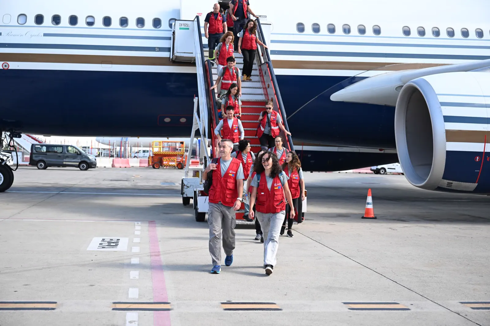 Sanitarios con chalecos rojos de la AECID bajan por la escalerilla de un avión en la pista de un aeropuerto