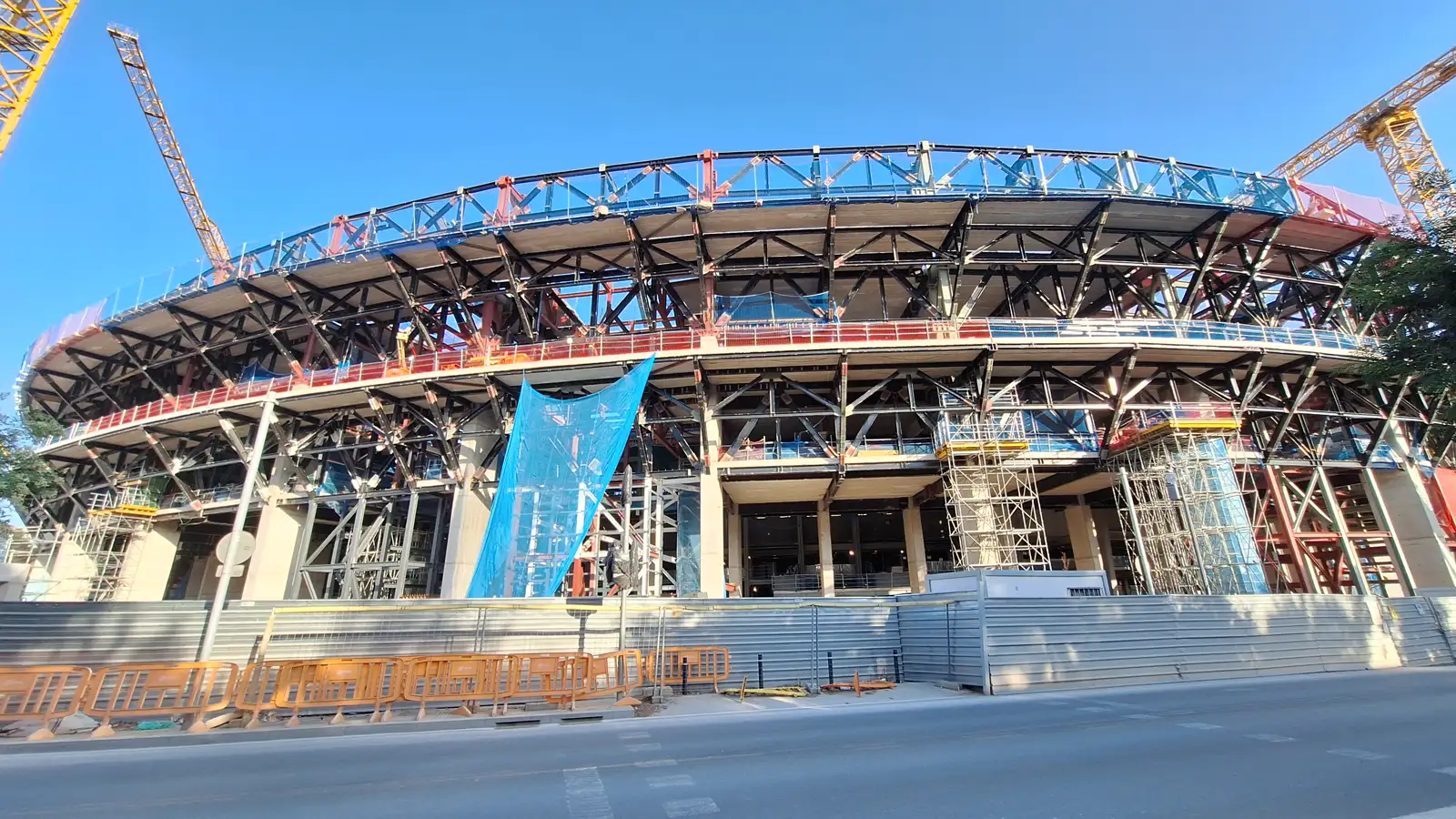 Exterior del Camp Nou en obras: la estructura metálica de las gradas al descubierto, andamios, grúas y vallas de obra en la acera.