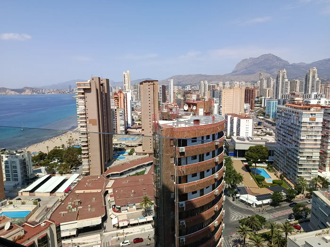 Vista aérea de bloques de hoteles y apartamentos junto a la playa de Levante de Benidorm, con el mar a la izquierda y montañas al fondo