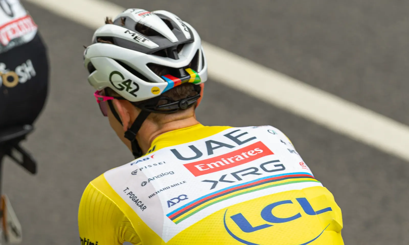 Tadej Pogacar, de espaldas sobre la bicicleta, con el maillot amarillo de líder del Tour de Francia y el nombre T. Pogacar impreso en la espalda.