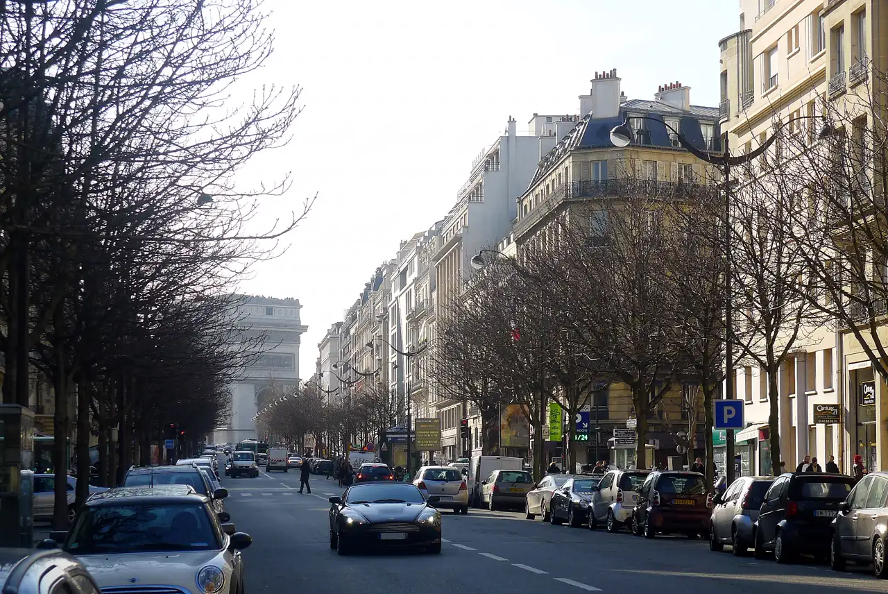 Avenida Hoche de París, con edificios haussmanianos de piedra clara a ambos lados, coches aparcados y el Arco del Triunfo al fondo entre árboles sin hojas