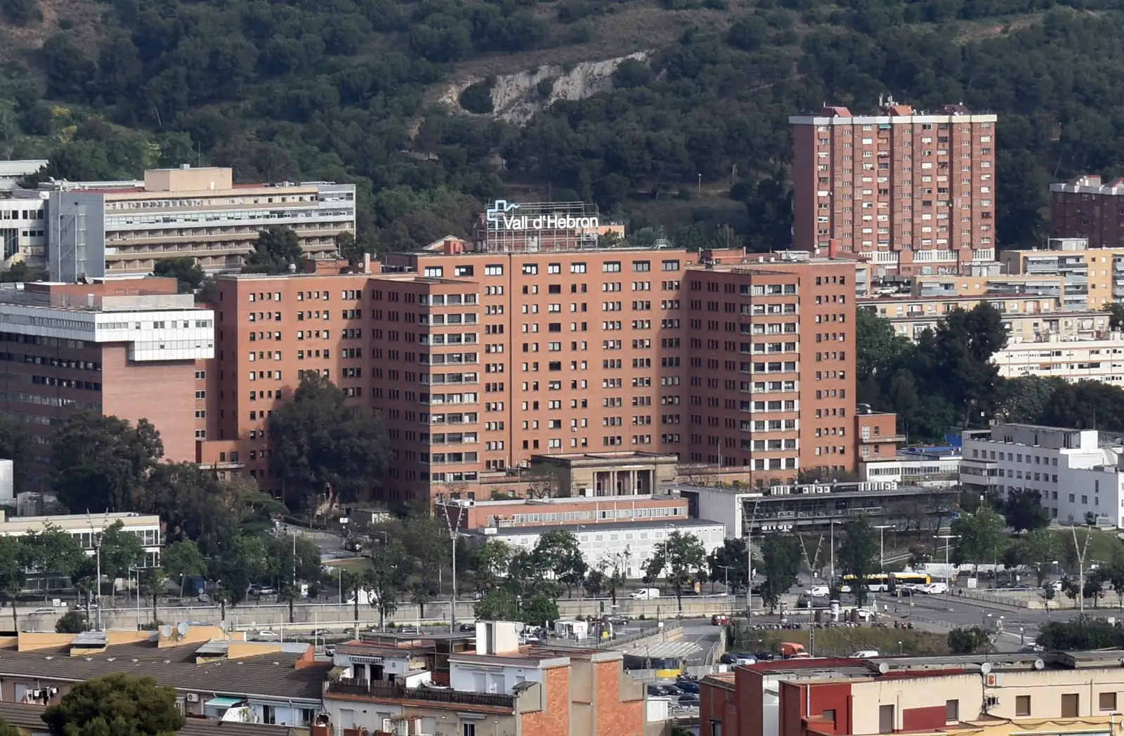 Vista a distancia del edificio principal del Hospital Vall d'Hebron de Barcelona, con su rótulo en la azotea y la sierra de Collserola al fondo