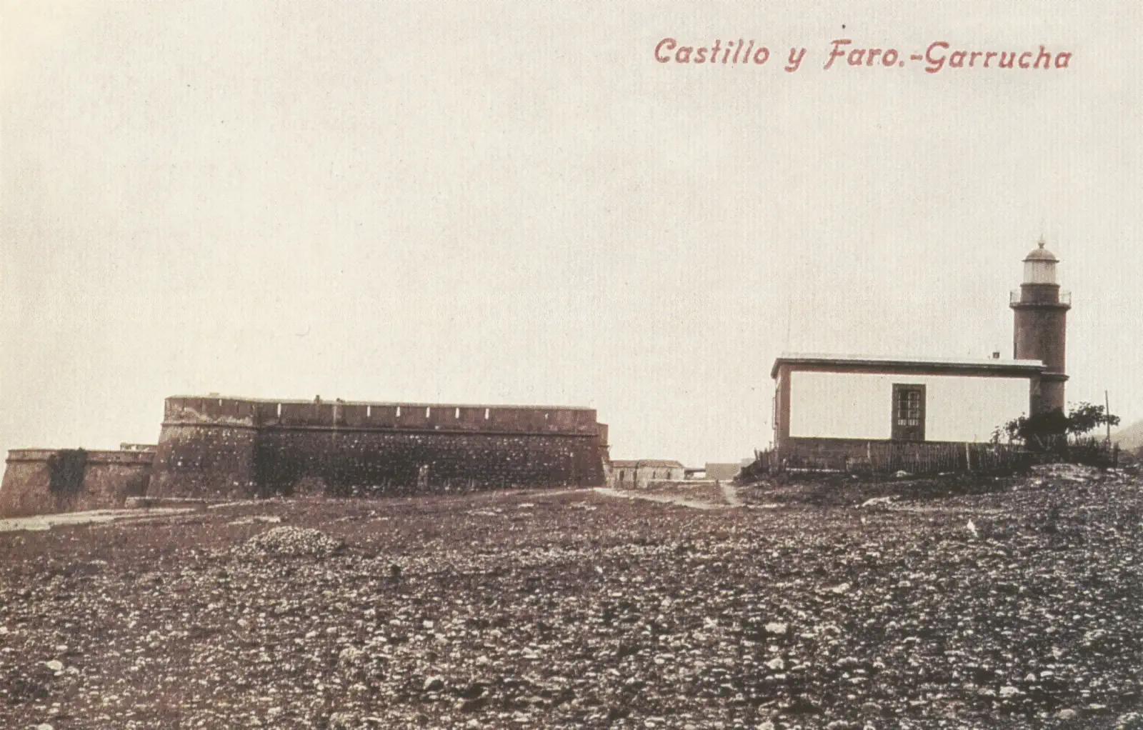 Postal antigua en tonos sepia: a la derecha, un edificio bajo y encalado con una torre cilíndrica de faro adosada; a la izquierda, la muralla de un castillo, sobre un terreno pedregoso.