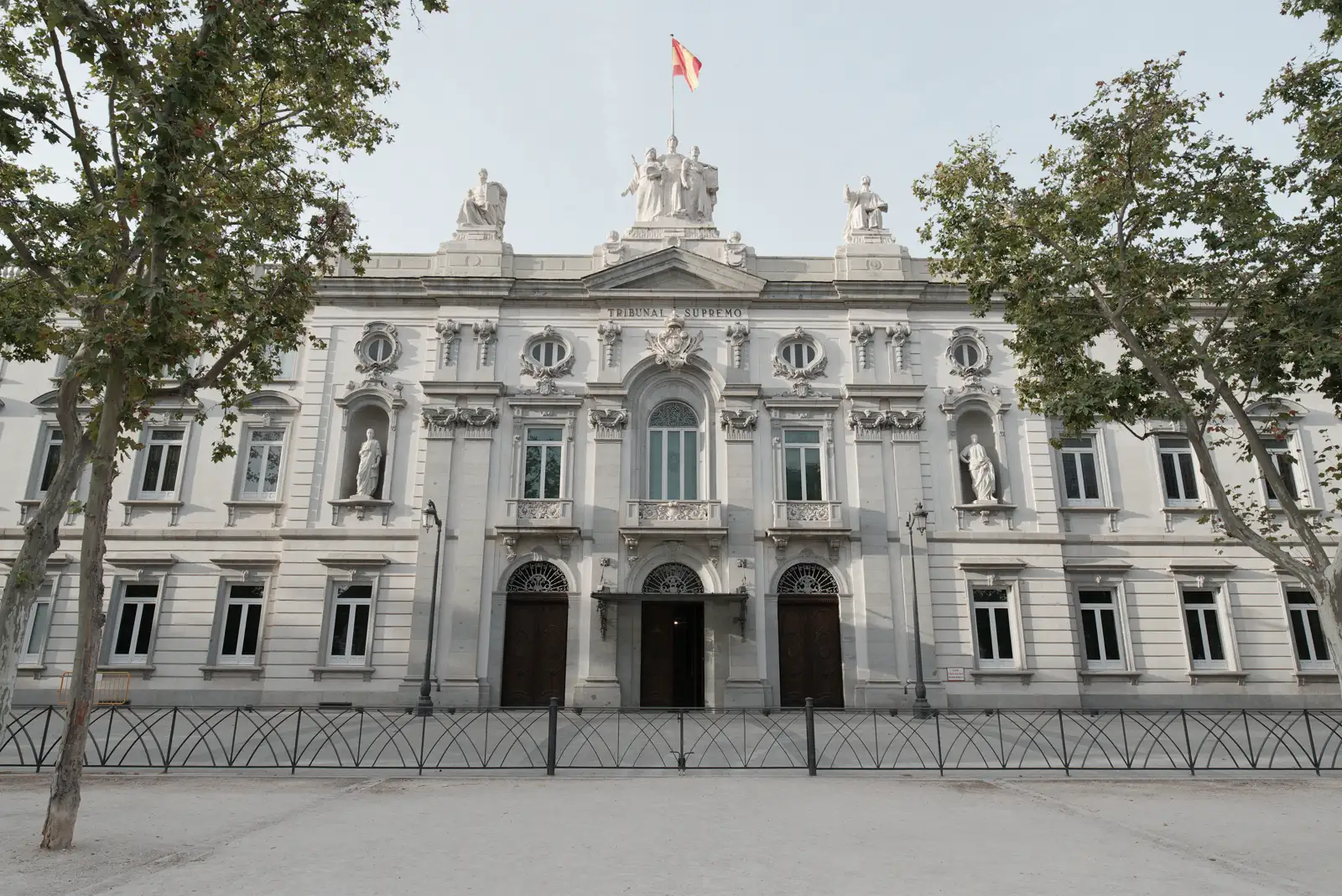 Fachada principal del edificio del Tribunal Supremo en Madrid, con la bandera de España ondeando sobre el frontón y árboles a ambos lados