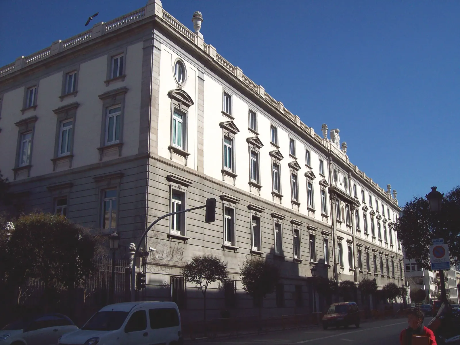 Fachada sur de piedra del edificio del Tribunal Supremo en Madrid, con su portada barroca y la torre del reloj, bajo un cielo azul.