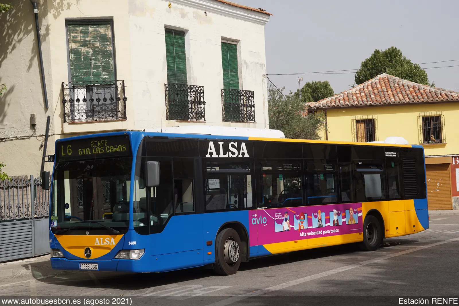 Autobús urbano azul y amarillo estacionado junto a un edificio de fachada clara, con el rótulo de destino «Renfe - Gta. Las Cañas» en el frontal y publicidad del servicio ferroviario Avlo en el lateral.