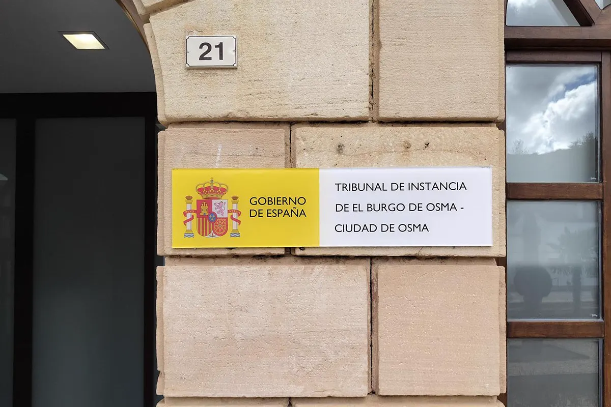 Placa con el escudo del Gobierno de España y el rótulo «Tribunal de Instancia de El Burgo de Osma - Ciudad de Osma», atornillada a la fachada de piedra del edificio junto al número 21.