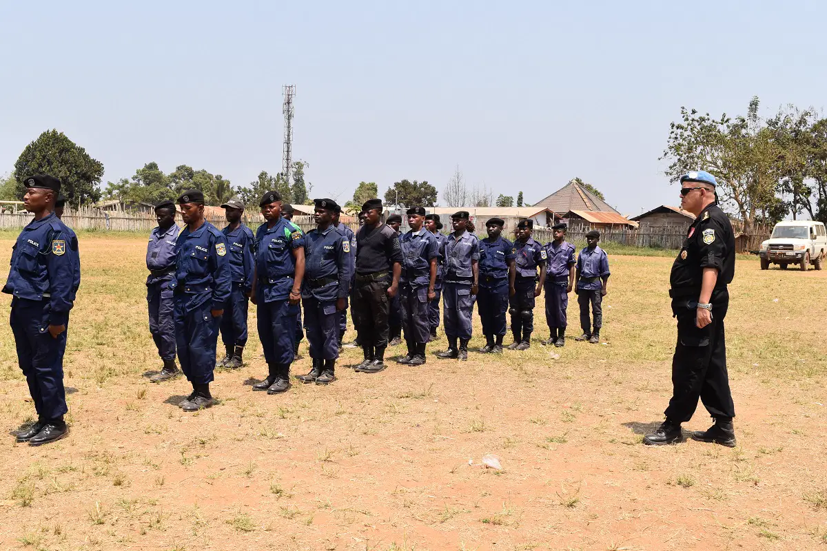 Una veintena de agentes de la Policía Nacional Congoleña, con uniforme azul y boina negra, formados en un descampado de tierra frente a un instructor con boina azul de la ONU