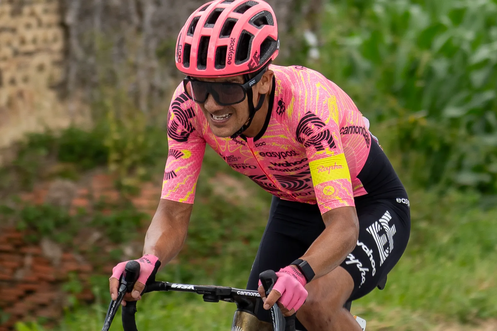 El ciclista Richard Carapaz, con el maillot rosa y amarillo del EF Education-EasyPost y casco rosa, pedalea agachado sobre el manillar durante una subida.
