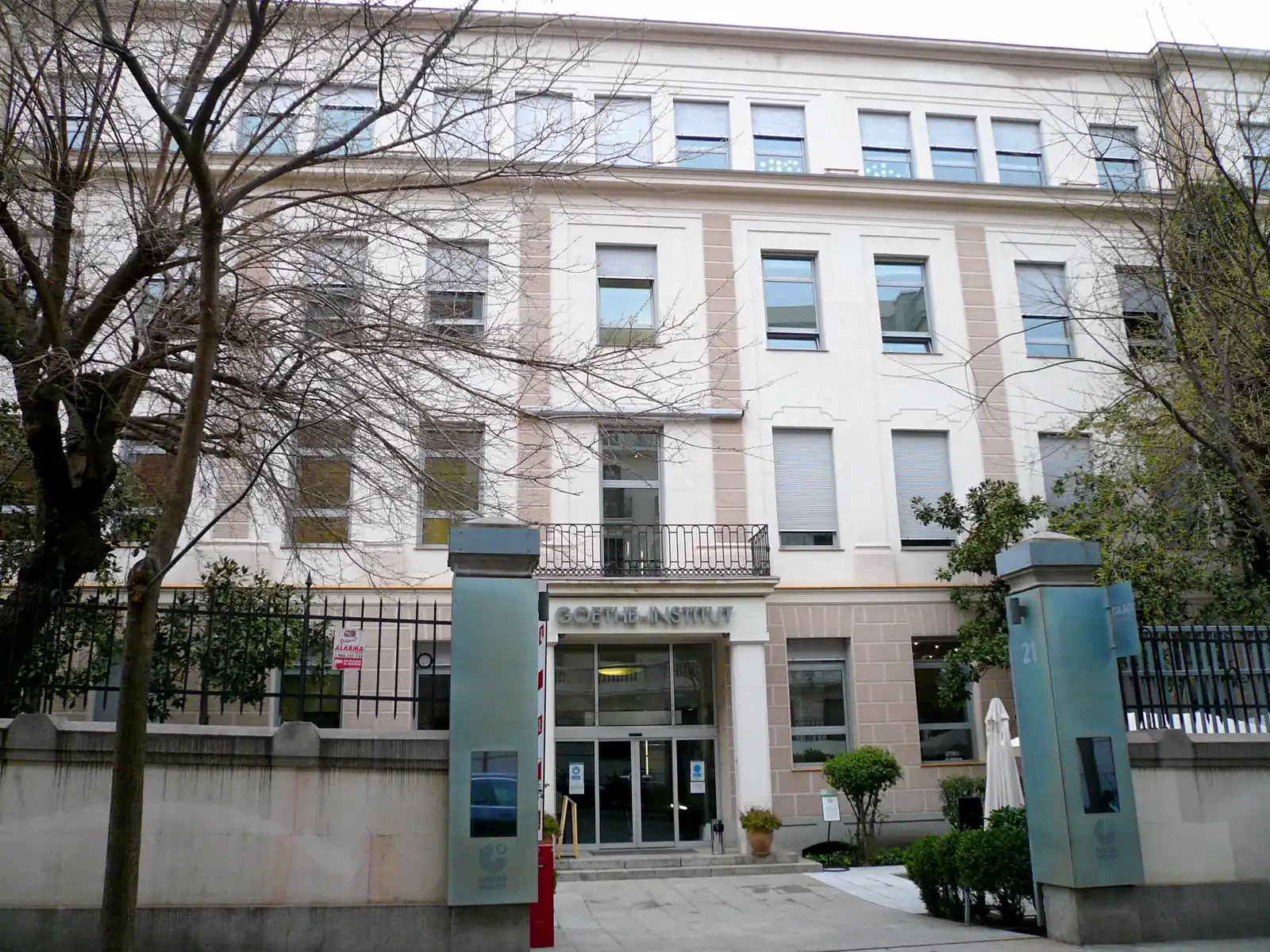Fachada blanca de cuatro plantas con el rótulo GOETHE-INSTITUT sobre la puerta acristalada de entrada, verja de hierro y árboles delante, en una calle de Madrid.