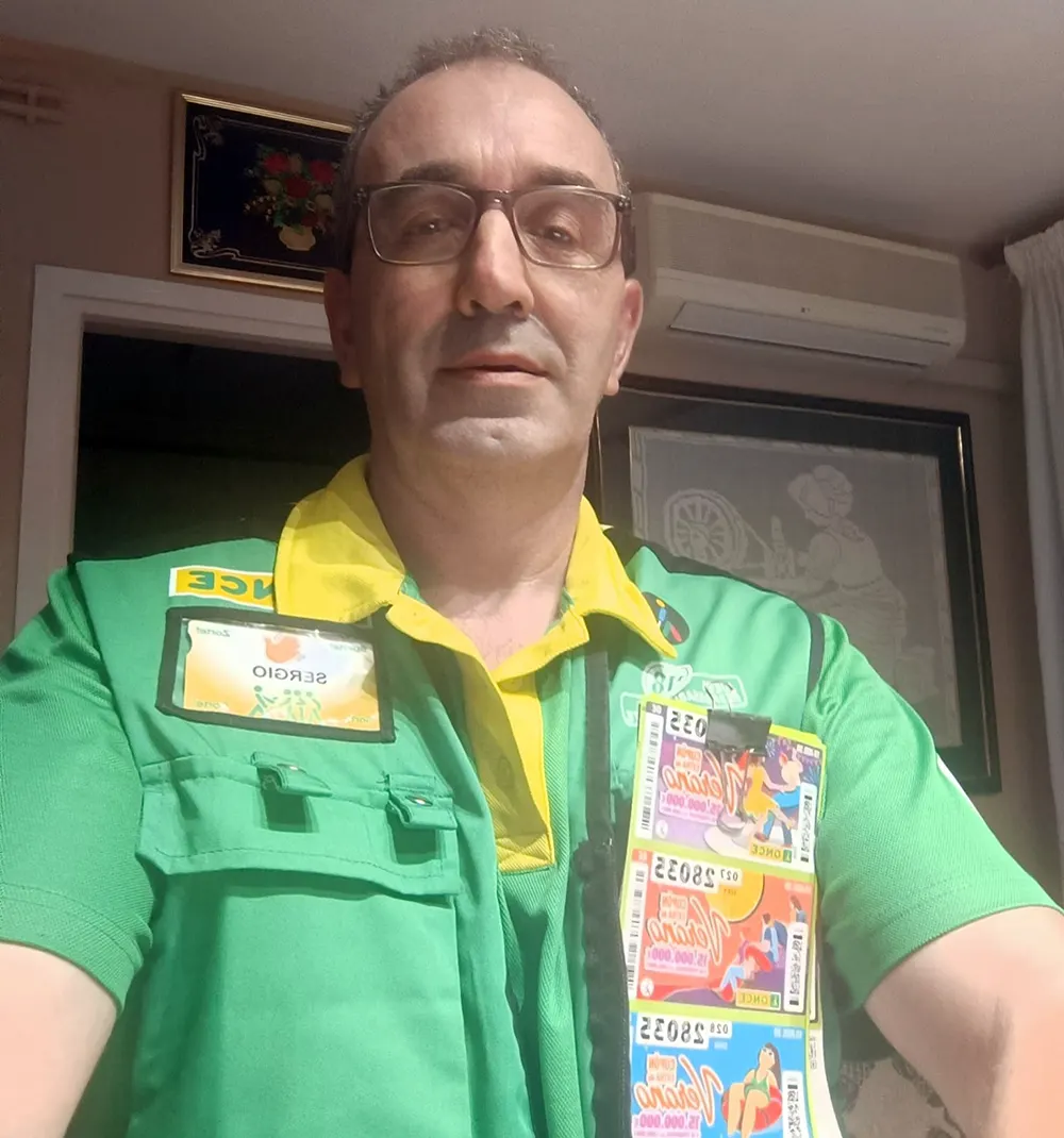 Sergio Martín Aznar, vendedor de la ONCE, con gafas y el chaleco verde y amarillo de la organización, con su tarjeta identificativa en el pecho y varios cupones colgados del bolsillo delantero