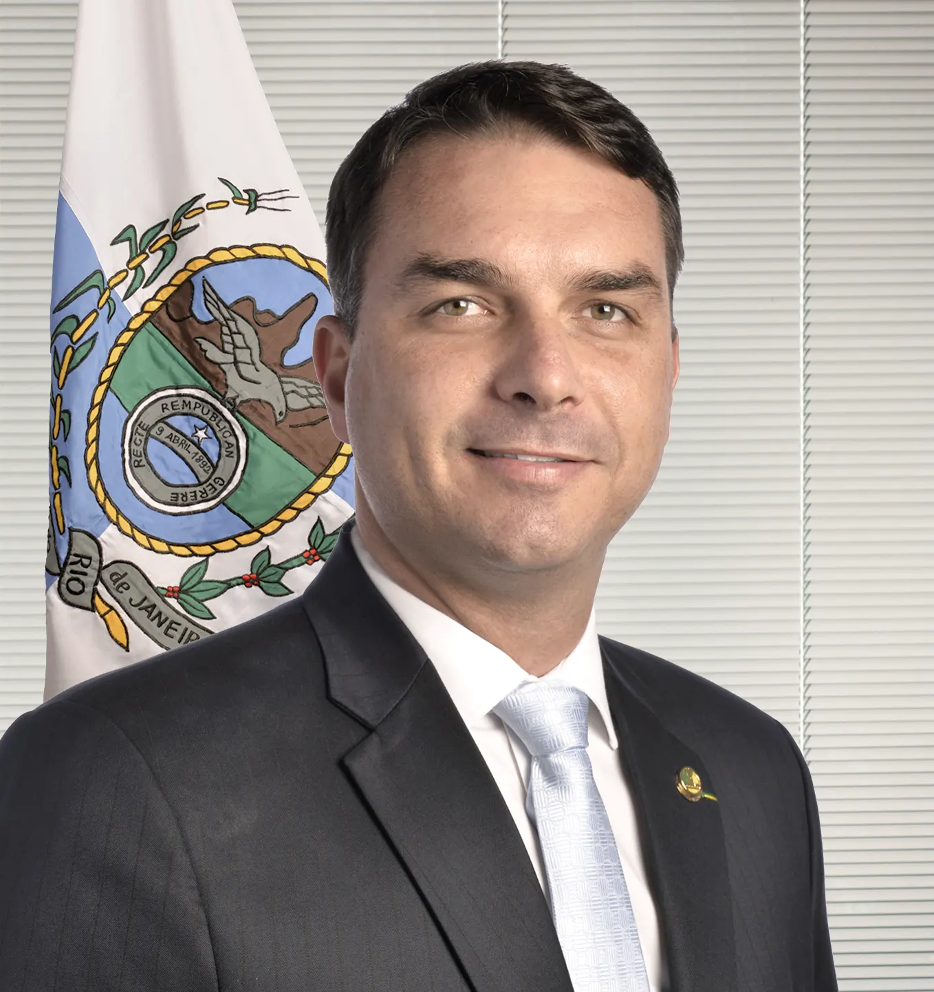 Retrato oficial del senador Flávio Bolsonaro, con traje oscuro y corbata clara, ante la bandera del estado de Río de Janeiro