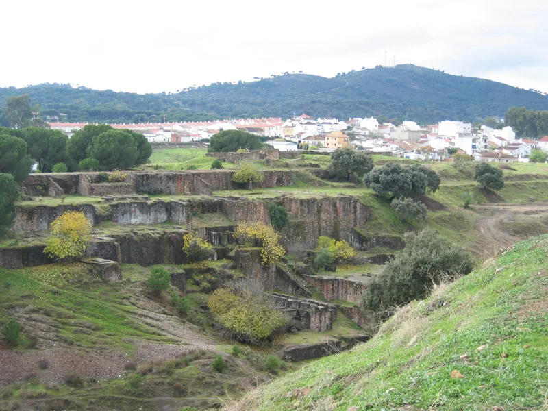 Vista de Cerro Muriano (Córdoba): las antiguas cortas mineras cubiertas de matorral y encinas en primer plano y, al fondo, el caserío blanco del poblado bajo las lomas arboladas de Sierra Morena.