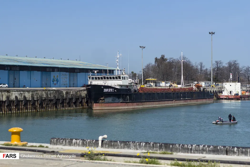 Buque de carga de casco negro con el nombre IRAN SEYR 1 pintado en la proa, amarrado junto a un almacén azul en un muelle del puerto de Nowshahr, en la costa iraní del mar Caspio.