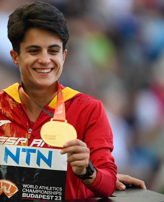 La marchadora María Pérez, con la equipación roja de la selección española, sonríe mientras sostiene con la mano derecha una medalla de oro colgada de una cinta.