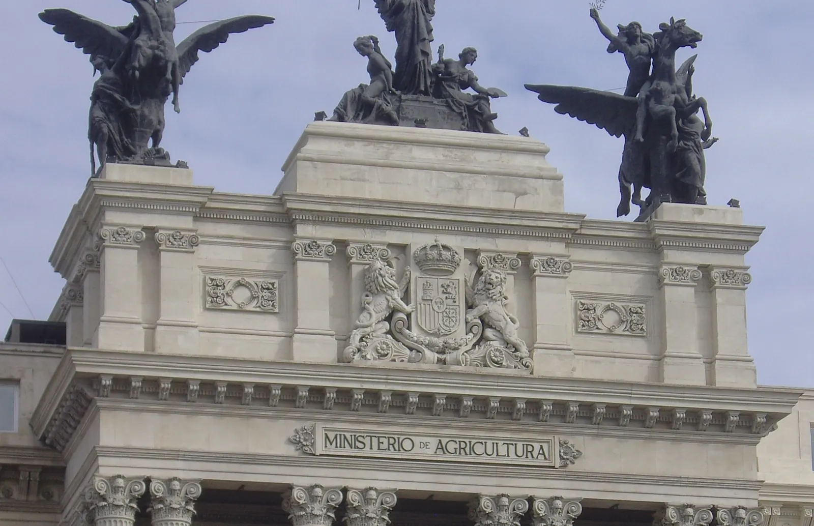 Fachada superior del edificio del Ministerio de Agricultura en Madrid, con el escudo de España, la inscripción «Ministerio de Agricultura» y el grupo escultórico de los pegasos de bronce sobre la cornisa.
