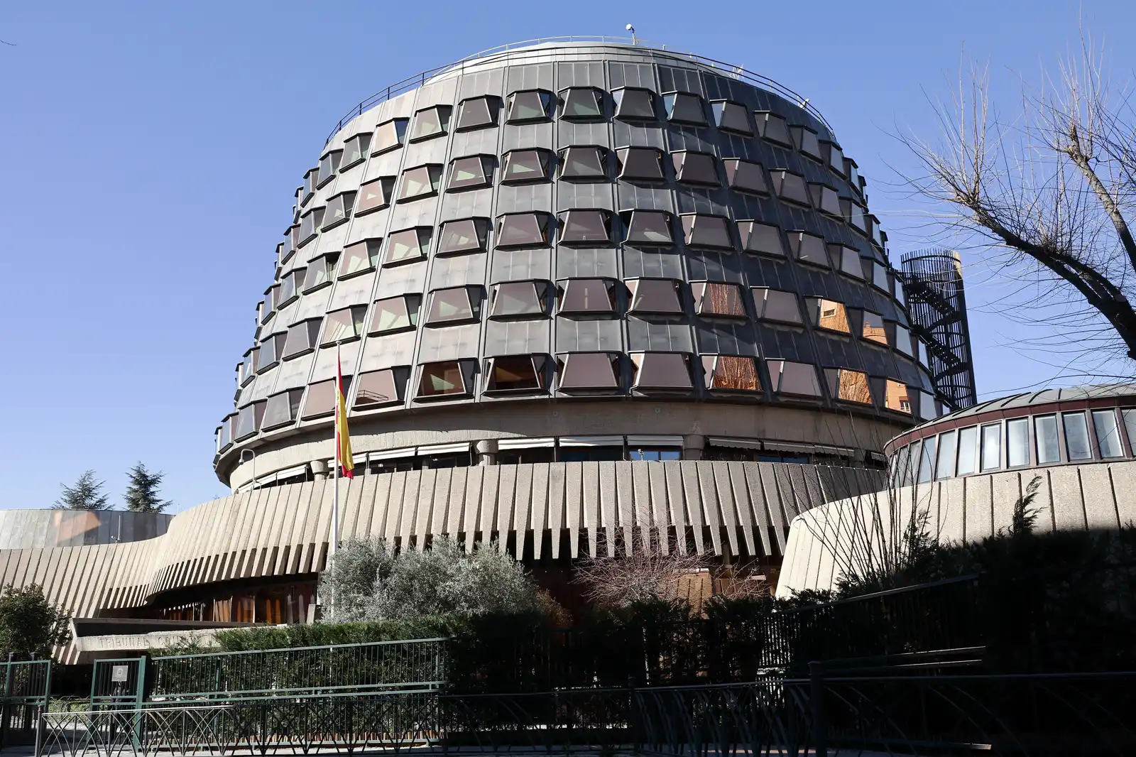 Fachada circular de vidrio y hormigón de la sede del Tribunal Constitucional en Madrid, con la bandera de España en un mástil ante la entrada