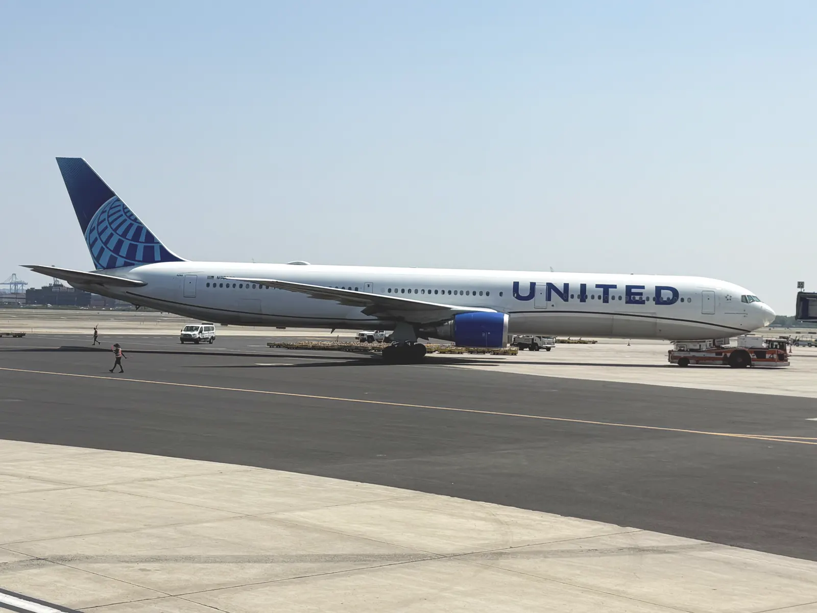 Avión Boeing 767 de United Airlines, blanco con el globo azul de la compañía en la cola, estacionado en la pista del aeropuerto de Newark con operarios y vehículos de tierra alrededor