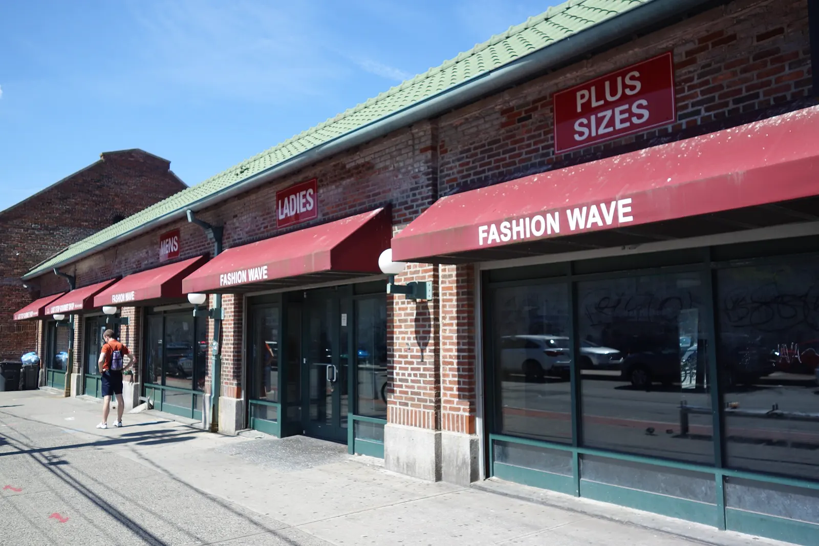 Hilera de comercios de ladrillo con toldos rojos junto a la acera de Beach 116th Street, en Rockaway Park (Queens, Nueva York), en un día soleado