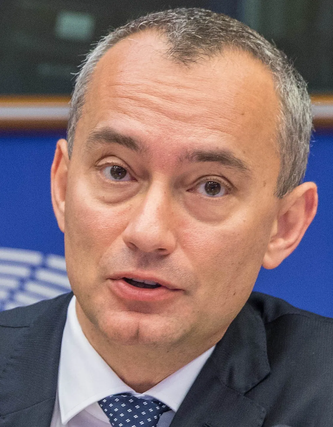 Primer plano del diplomático búlgaro Nickolay Mladenov, de pelo canoso, traje oscuro, camisa blanca y corbata azul de topos, hablando ante un fondo azul
