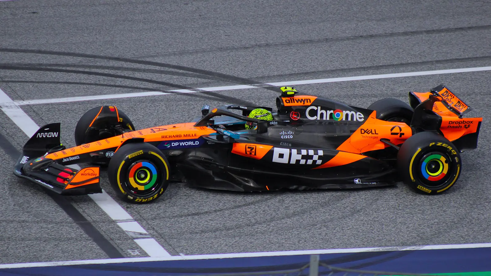 Monoplaza de McLaren, naranja y negro, con el número 4 y un piloto de casco amarillo flúor, rodando sobre el asfalto de un circuito.