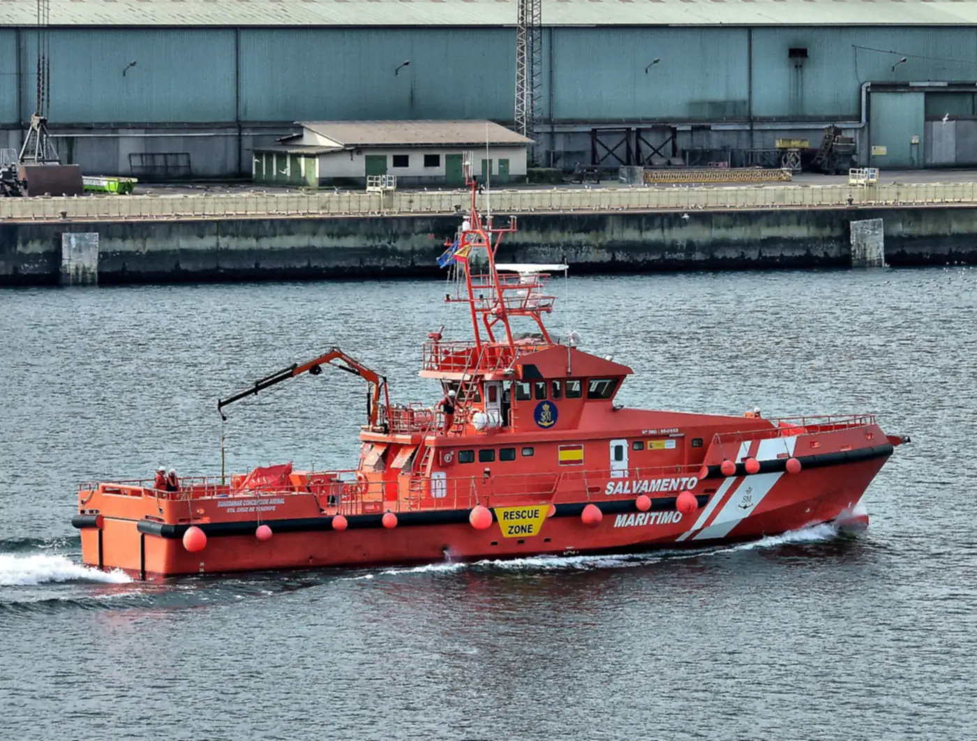 Buque naranja de Salvamento Marítimo, el Guardamar Concepción Arenal, navegando junto a un muelle industrial en el puerto de A Coruña.