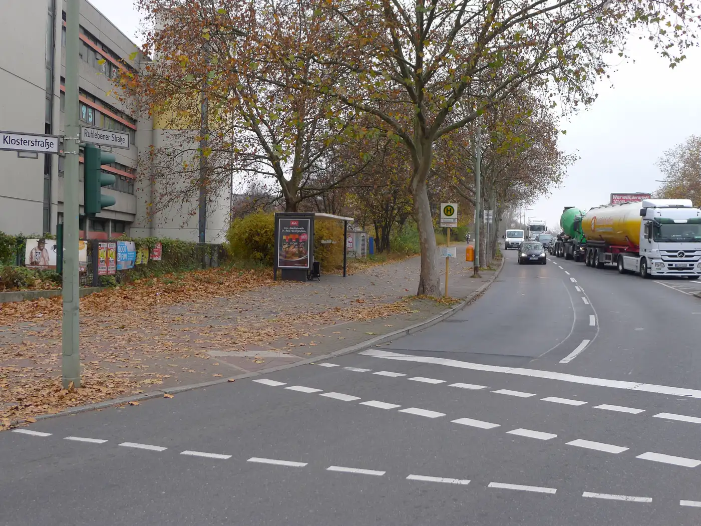 Cruce de la Ruhlebener Straße con la Klosterstraße, en el distrito berlinés de Spandau: una avenida de varios carriles con camiones y coches circulando, una marquesina de autobús, plátanos de sombra sin apenas hojas y hojarasca de otoño en la acera.