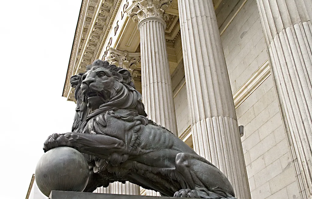 Uno de los leones de bronce de la entrada del Congreso de los Diputados, con una pata sobre una bola, ante las columnas de la fachada principal del edificio.