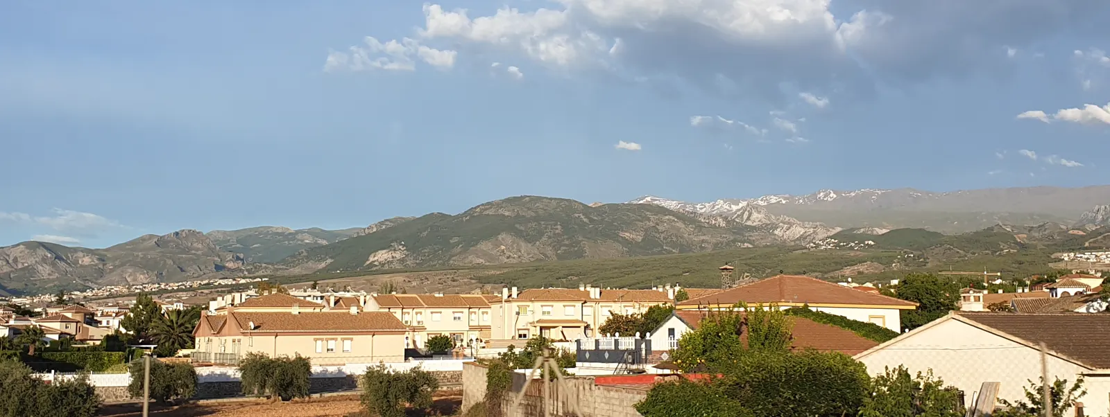 Vista panorámica del casco urbano de Ogíjares desde la autovía GR-30, con bloques de viviendas y casas bajas extendidos sobre la llanura de la Vega de Granada y las estribaciones de la sierra al fondo.