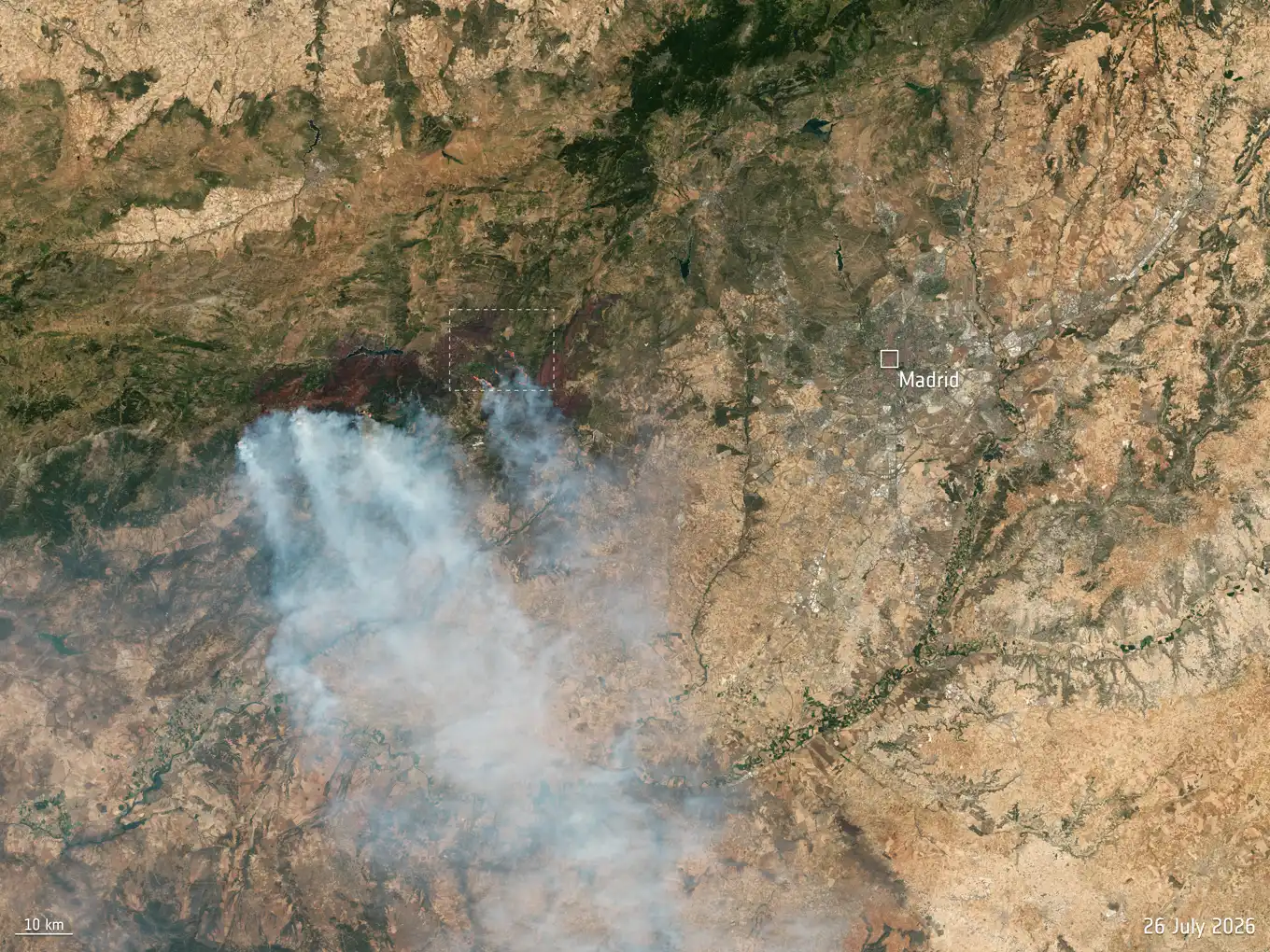 Imagen de satélite del centro peninsular: sobre un mosaico de tierras ocres y manchas verde oscuro se extiende una gran cicatriz parda al oeste de Madrid, de la que salen varias columnas de humo blanco arrastradas hacia el suroeste; a la derecha se distingue la mancha gris de la ciudad, rotulada «Madrid», y abajo la escala de 10 kilómetros y la fecha, 26 de julio de 2026.