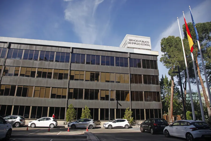 Fachada acristalada de un edificio administrativo de cuatro plantas en Madrid con el rótulo «Servicio Público de Empleo Estatal» en el cuerpo superior; a la derecha ondean las banderas de España y de la Unión Europea y en primer plano hay coches aparcados.