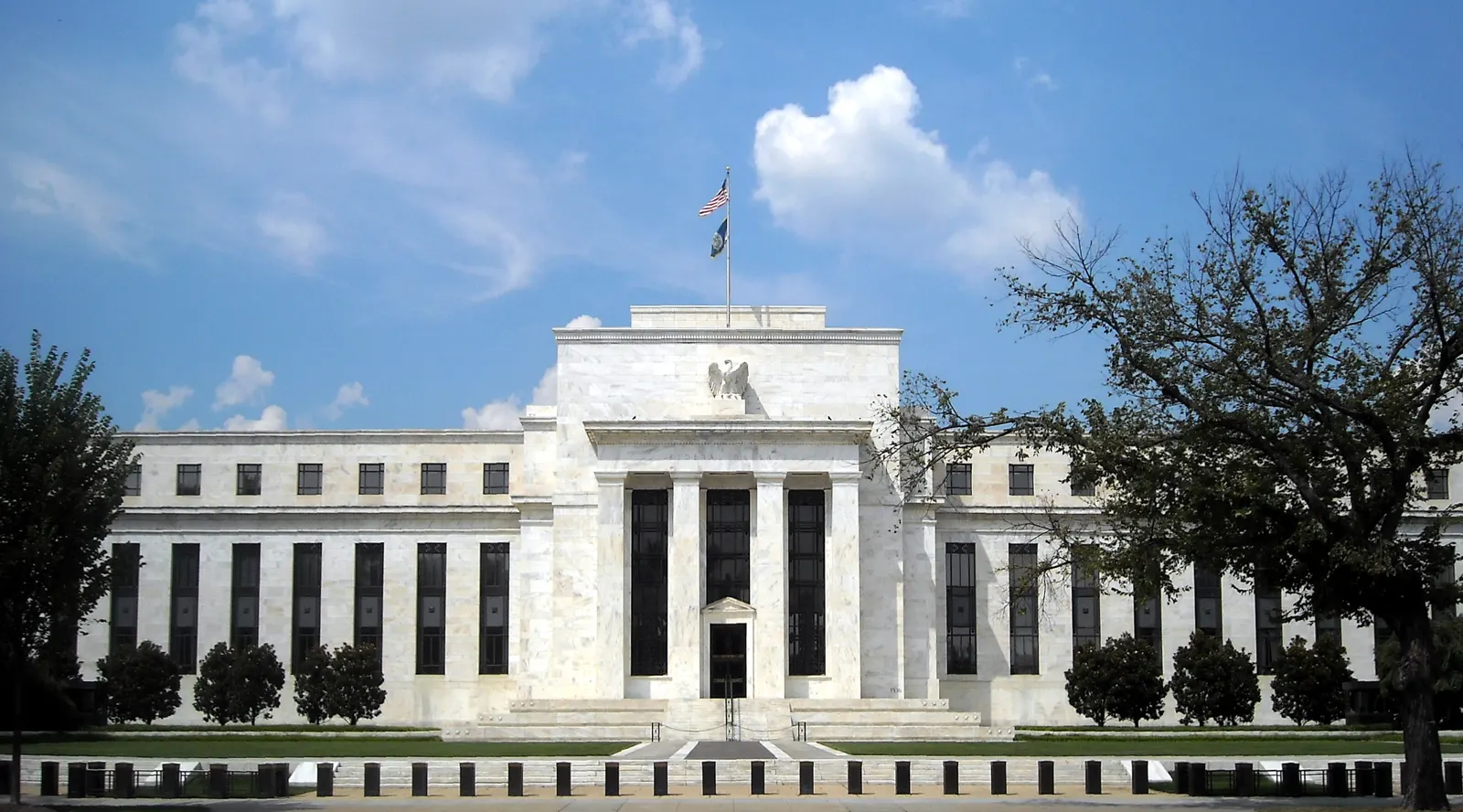 Fachada neoclásica de mármol blanco del edificio Marriner S. Eccles, sede de la Reserva Federal, en Washington, con banderas de Estados Unidos