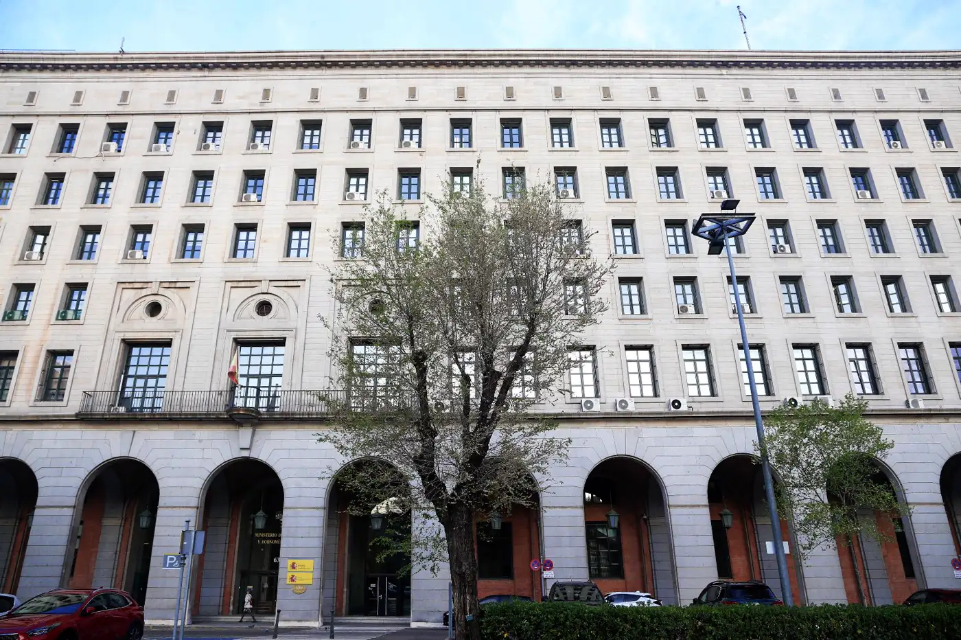 Fachada de piedra clara del Ministerio de Trabajo en el Paseo de la Castellana de Madrid, con seis alturas de ventanas, soportales de arcos en la planta baja y un árbol en primer término