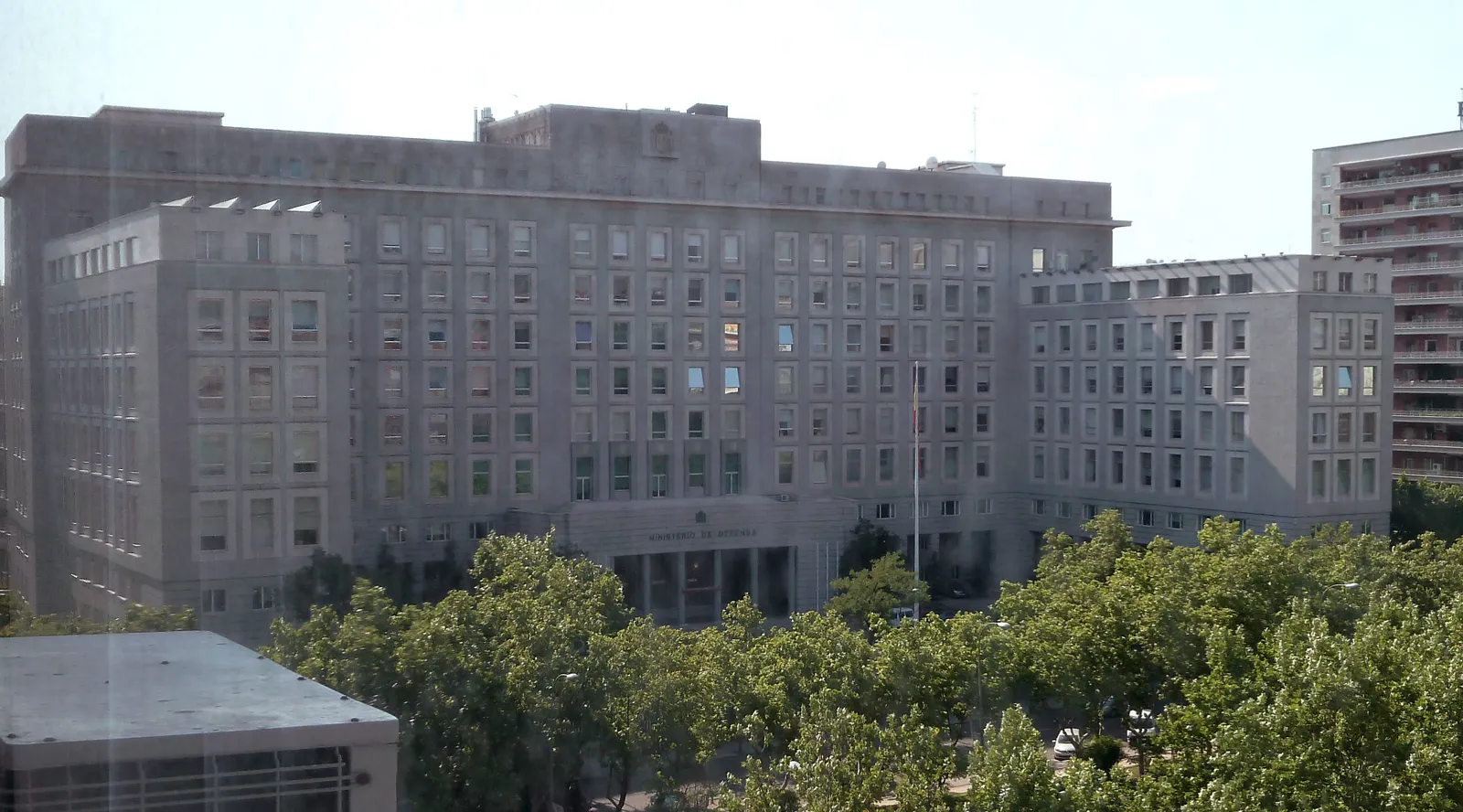 Fachada del edificio del Ministerio de Defensa en el paseo de la Castellana de Madrid, un bloque gris de siete plantas con ventanas cuadradas, el rótulo «Ministerio de Defensa» sobre la entrada principal y arbolado delante.
