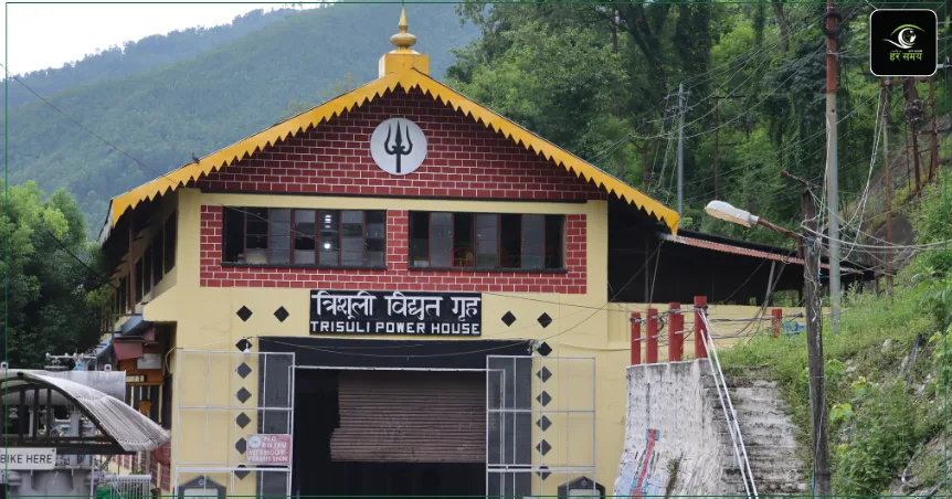 Casa de máquinas de la central hidroeléctrica de Trishuli: un edificio amarillo de dos plantas con remates rojos, tejado a dos aguas de borde dorado y un tridente pintado en el frontón, con el rótulo «Trisuli Power House», al pie de una ladera boscosa