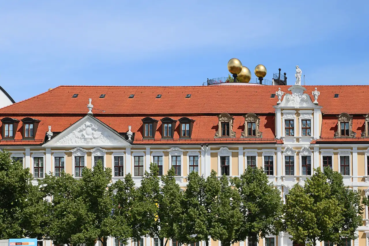 Fachada barroca de color crema y blanco del edificio del Landtag de Sajonia-Anhalt en Magdeburgo, con tejado de teja roja, árboles delante y cielo azul al fondo.