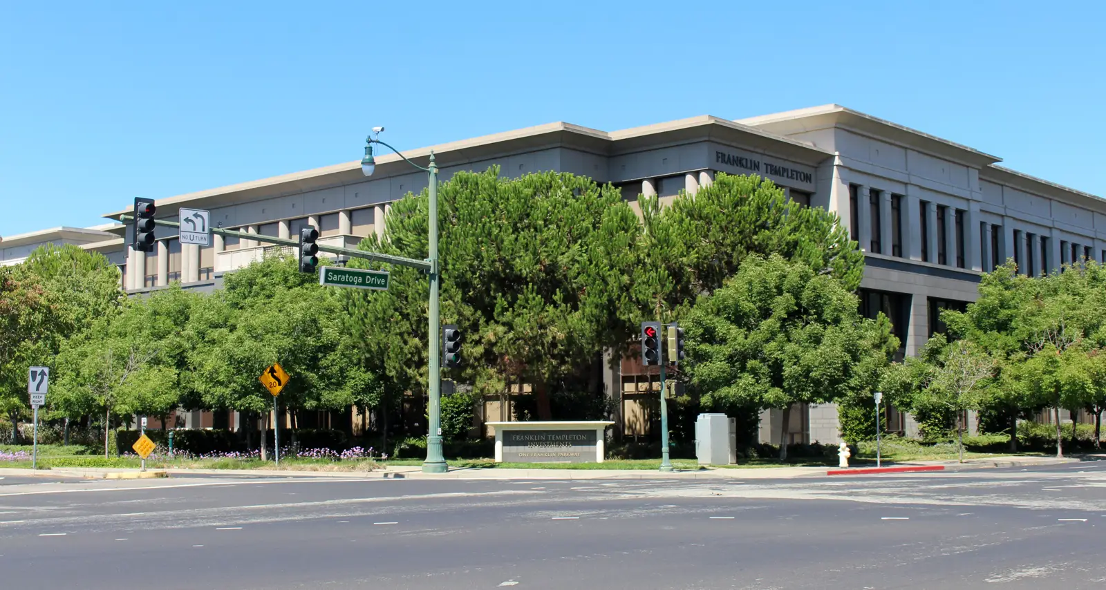 Edificio de oficinas de varias plantas rodeado de árboles, con el rótulo Franklin Templeton en la fachada y un monolito con el nombre de la empresa junto a la acera.