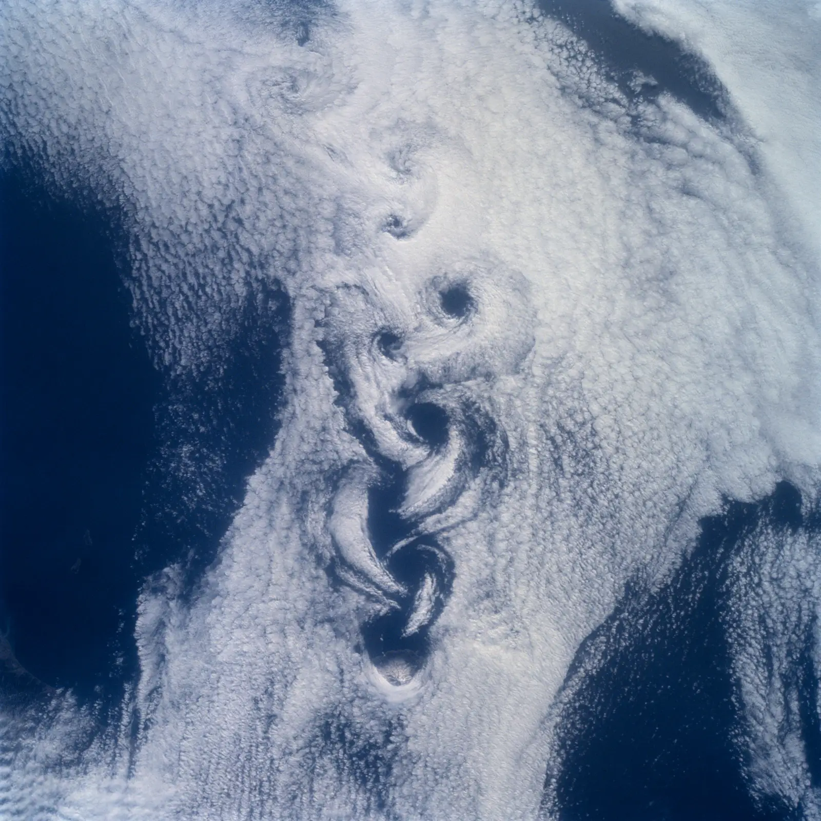 Vista desde el espacio de una masa de nubes blancas sobre un océano azul oscuro, con una hilera de remolinos alineados en espiral